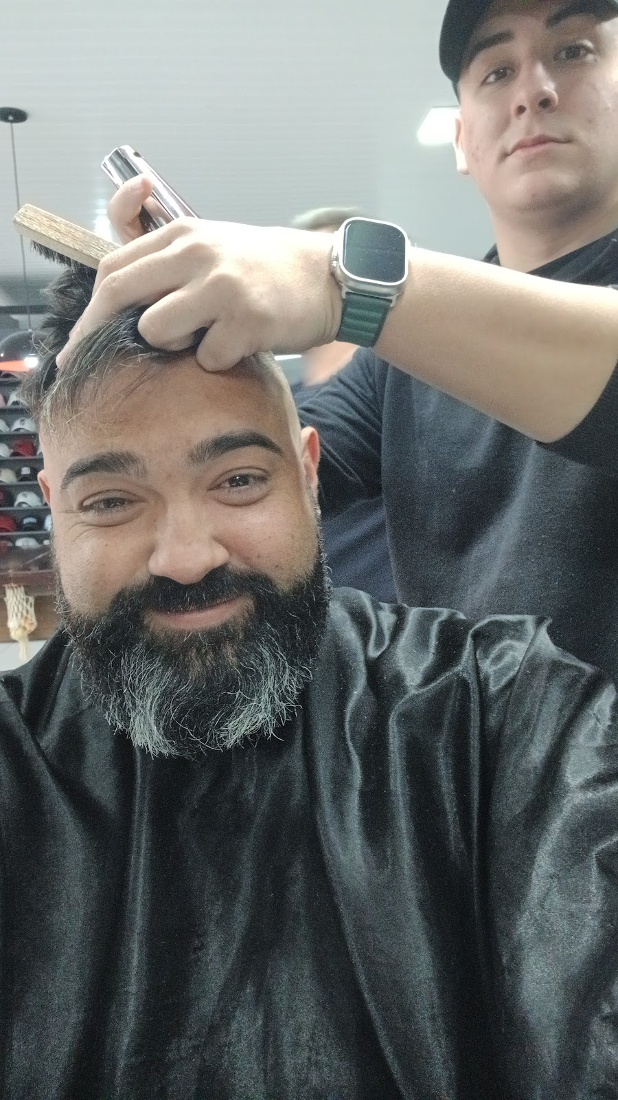 Cliente sorrindo durante o corte, com o barbeiro ao fundo, na Barbearia Império Ferreira